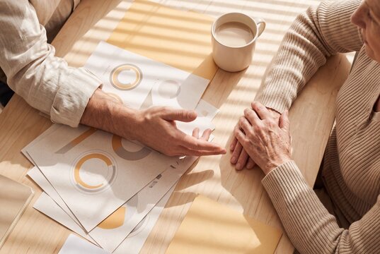 High Angle View of Financial Advisor Explaining Investment Documents to Senior Woman at Wooden Table