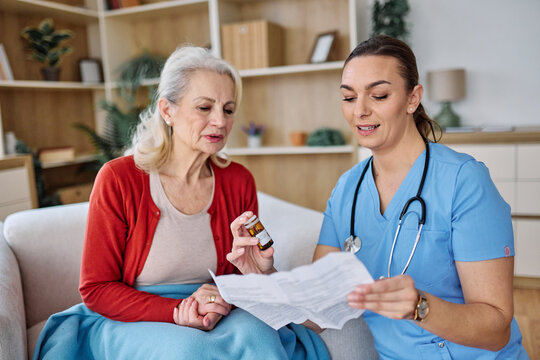 Doctor or nurse caregiver showing a prescrption or documents and holding drug bottle to senior woman at home or nursing home