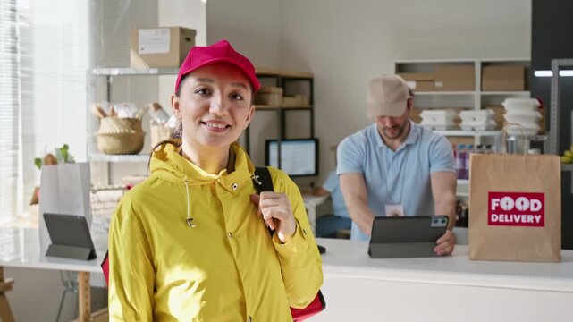 Portrait of young Caucasian female courier holding thermal backpack at food pickup hub. Footage ideal for promoting online takeout apps, express meal ordering and retail delivery services