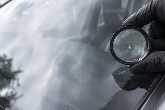 Inspecting windshield stone chip with magnifying glass