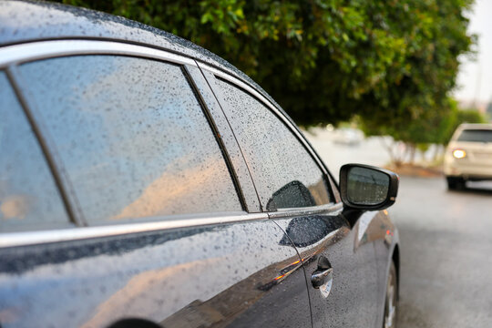 Close up of raindrops on Navy blue color car side window and mirror during rainy weather, ideal for automotive