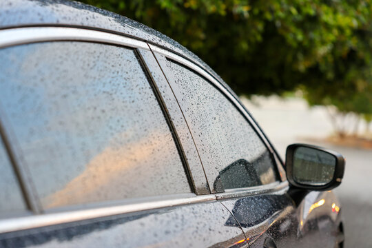 Close up of raindrops on Navy blue color car side window and mirror during rainy weather, ideal for automotive