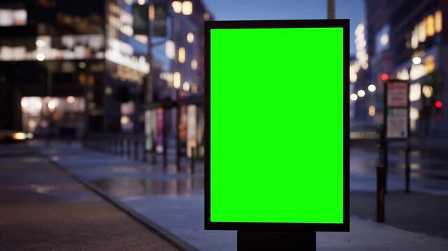 Blank green screen city light billboard on a metropolitan street at night with glowing windows and street lights, clear sky. Timelapse of passing traffic with shallow depth of field and soft bokeh