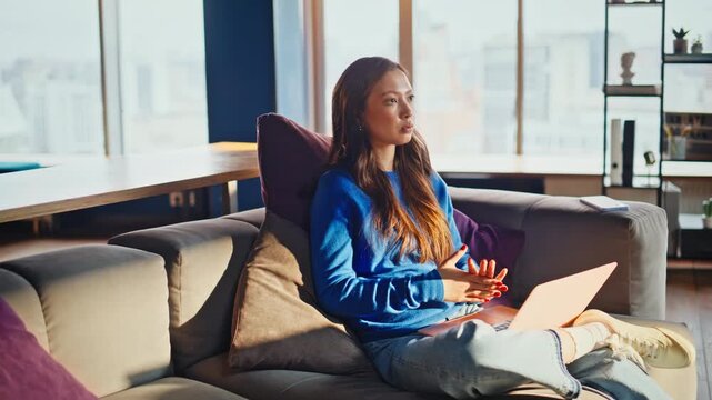 Woman resting laptop work looking window. Pensive remote employee couch loft.