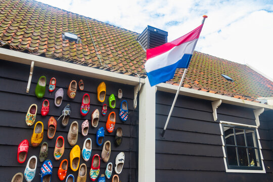 National flag of the Netherlands waving on a traditional wooden house wall decorated with colorful clogs under a tiled roof in Zaanse Schans, Netherlands