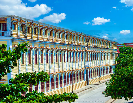 Historic yellow colonial building with beautiful arched windows and balconies in Cartagena, Colombia, framed by green trees under a blue sky.