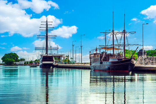 Historic wooden galleon ships anchored in the beautiful harbor of Cartagena, Colombia under a sunny blue sky with reflections on the water.