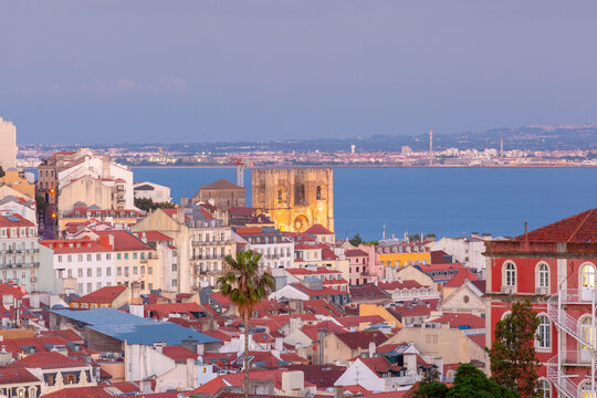 Lisbon skyline with the illuminated cathedral, traditional red rooftops and the Tagus River during sunset, Portugal.