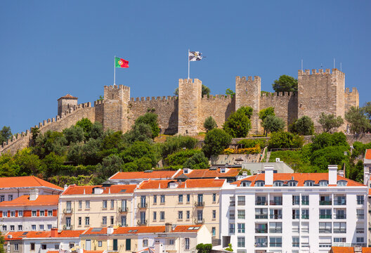 Historic stone fortifications rise above residential buildings and red tiled roofs in central Lisbon, Portugal.