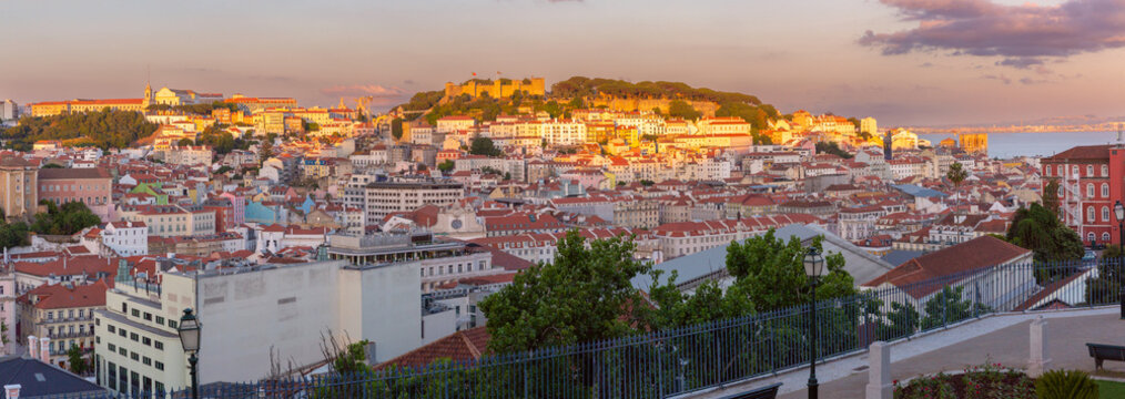 Panoramic cityscape of Lisbon with historic architecture and red rooftops illuminated by warm sunset light, Portugal.