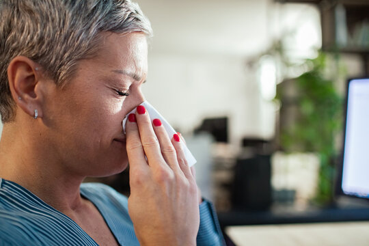 Ill woman blowing her nose in modern office