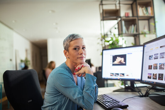Confident female designer working at dual monitors in modern office