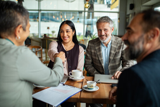 Smiling business colleagues shaking hands during meeting in cafe