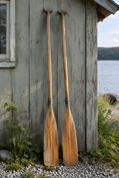 Pair of wooden oars propped against a weathered lakeside shed wall with peeling paint