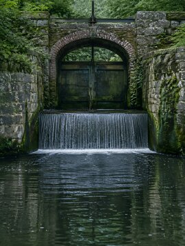 Old stone sluice gate and weir pool on a lowland river with mossy brick arch and water sheeting over