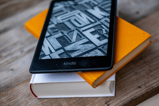modern Kindle e reader on stack paper books, black e-book reader, digital book Kindle, tablet computer device displaying text electronically, electronic paper technology, reading fiction, text editing
