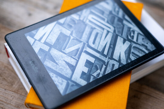 modern Kindle e reader on stack paper books, black e-book reader, digital book Kindle, tablet computer device displaying text electronically, electronic paper technology, reading fiction, text editing