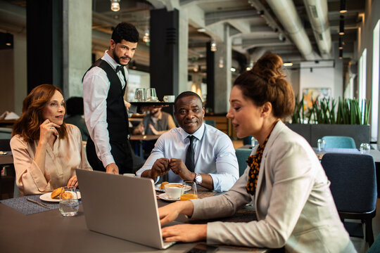 Business colleagues meeting with laptop in a cafe while a waiter serves