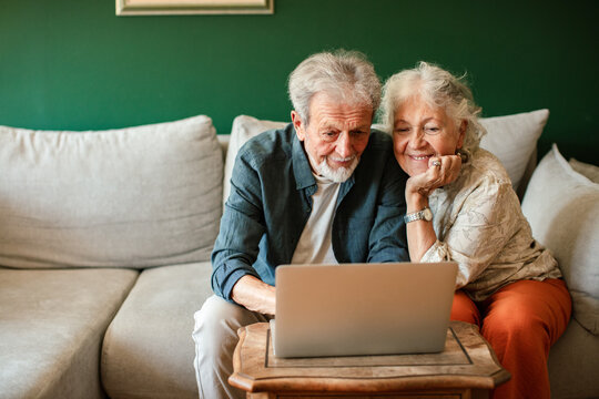 Happy senior couple browsing laptop on living room sofa