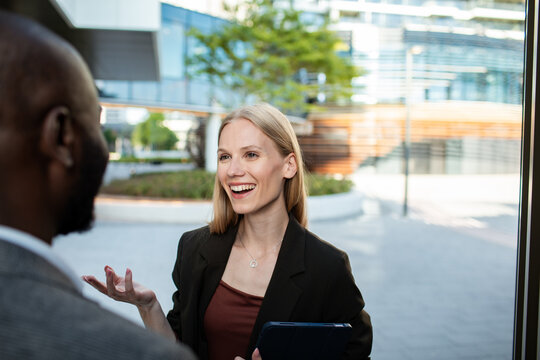 Smiling businesswoman talking with colleague outside modern office