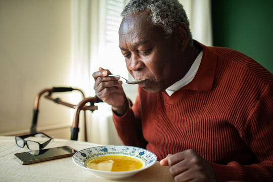 Senior man eating hot soup at home dining table