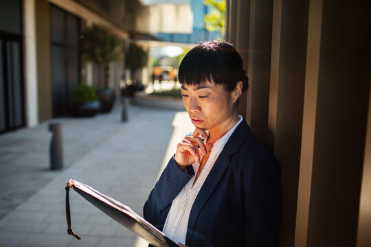 Businesswoman reviewing documents in sunlit office courtyard