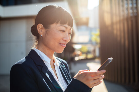 Smiling businesswoman using smartphone outdoors in city