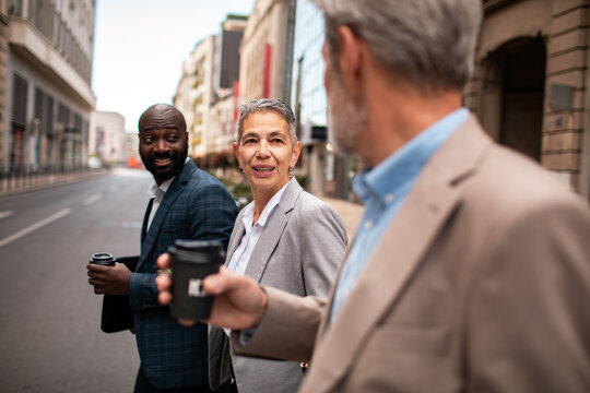 Three business colleagues walking and talking with coffee on a city street