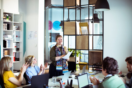 Team applauding female colleague after presentation in modern office