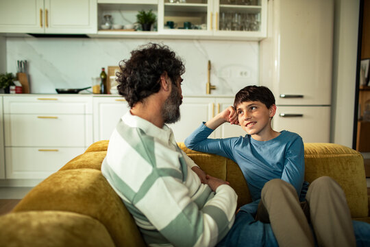 Father and son talking on sofa in modern home kitchen