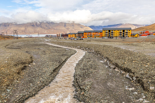 Summer view of Longyearbyen with meltwater stream crossing barren tundra, colorful apartment buildings and cloud-covered Arctic mountains, Longyearbyen, Spitsbergen, Svalbard, Norway