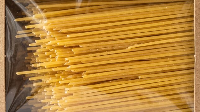 Uncooked spaghetti pasta packaged inside a brown cardboard box with a transparent plastic viewing window against bright studio background.