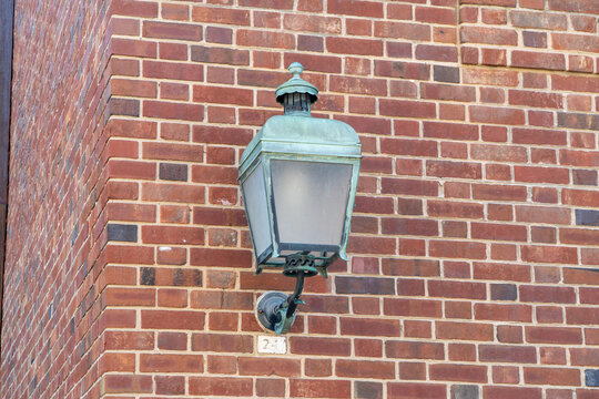 Vintage copper patina wall lantern on a textured red brick building exterior, featuring classic architectural details and an old number 24 plaque.
