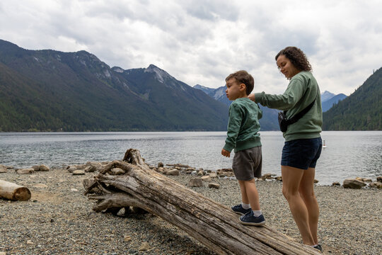 Mother And Son Exploring Driftwood On Rocky Shore At Chilliwack Lake, BC Canada With Mountains