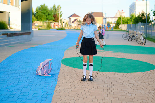 A young schoolgirl jumping rope outdoors near the school building
