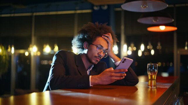 Tired african american man leaning head phone bar counter. Beer glass evening.