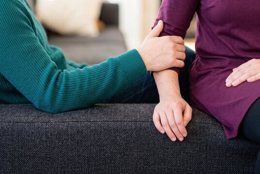 Close-up of a man comforting and holding a woman's arm while sitting together on a sofa, expressing empathy, care, and support