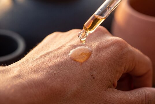 Close up view of applying cosmetic golden serum with a glass dropper pipette onto the back of a hand for skincare treatment