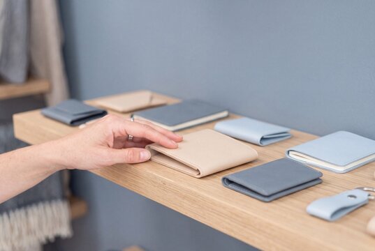 Customer choosing a handcrafted beige leather wallet on a wooden display shelf in a modern boutique shop