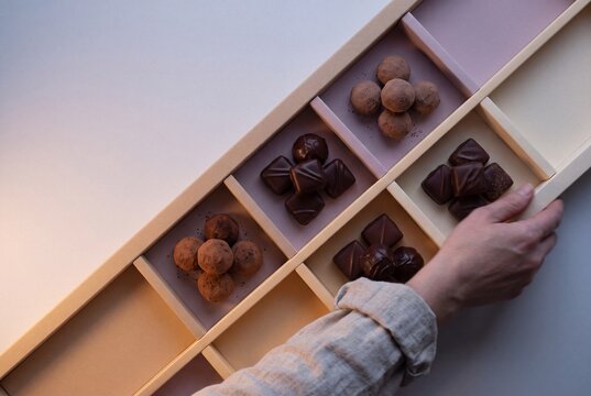 Hand opening an elegant luxury gift box filled with assorted chocolate truffles and artisan bonbons
