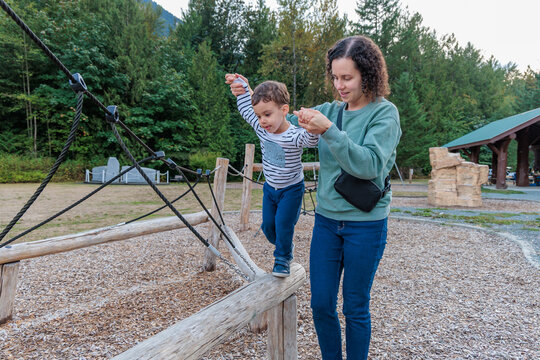 Mother Helping Young Son Balance on Wooden Playground Log at Park in Chilliwack, BC Canada