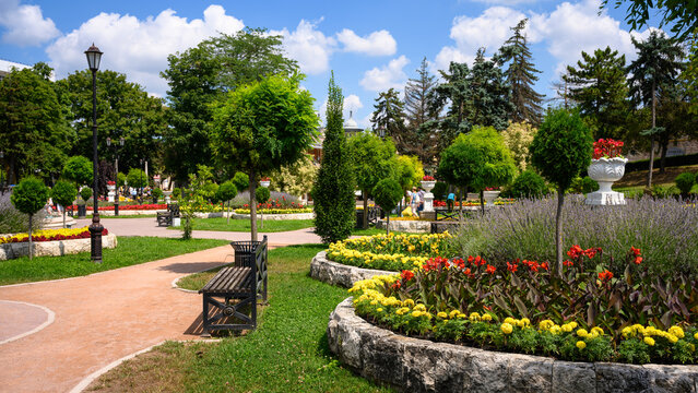 Landscaped public park with vibrant flower beds and green lawns on a sunny day, Pyatigorsk, Russia. Urban botanical garden featuring walking paths, metal benches, and manicured trees in summer