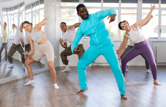 Cheerful adult African American man learning to dance krump with group in modern choreographic studio..