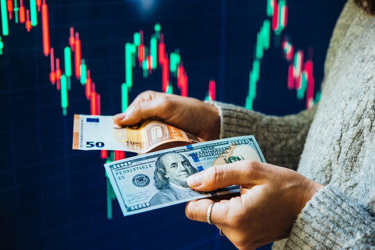 US dollars and euros in front of the stock exchange screen showing trading graphics.