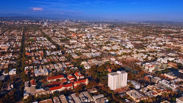Sunlit densely populated green cityscape of modern Los Angeles, California, USA. Drone flight over the city approaching the mountains.