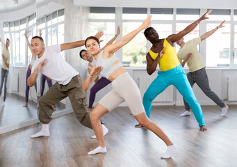 Fototapeta premium Happy emotional sporty young female dancer rehearsing popping techniques during group workout in modern street dance studio