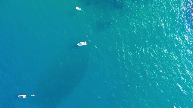 Small boats resting at anchor on bright blue sea, sunlight shimmering across the surface and dark seagrass patches visible beneath, a calm bay seen from above, concept of tranquil holidays, sailing a