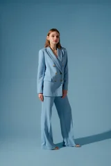 Beautiful fashionable woman wearing trendy blue color trouser suit, pantsuit, posing on blue background. Full-length studio fashion portrait. Copy, empty space for text © Victoria Fox