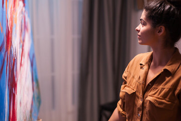 Close side profile of an artist looking carefully at a colorful abstract canvas, focused on the artwork during a quiet pause in the creative process, highlighting evaluation and observation. © DC Studio