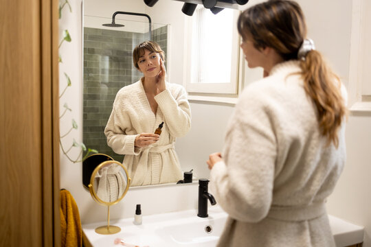 Woman applying skincare serum in bathroom mirror
